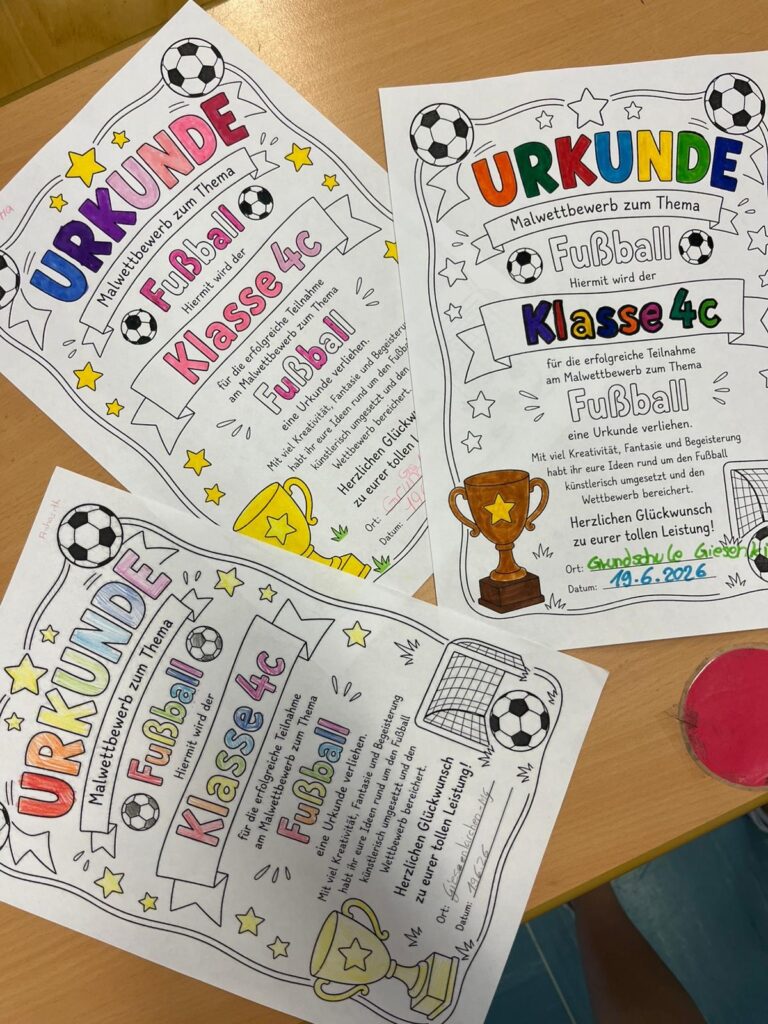Auf einem blauen Tisch liegen drei bunte, handverzierte Urkunden mit dem Titel „Urkunde für den Fußballwettbewerb der Klasse 4cs“. Jede Urkunde ist mit Abbildungen von Fußbällen, einem Pokal, Sternen und einem Tor verziert.