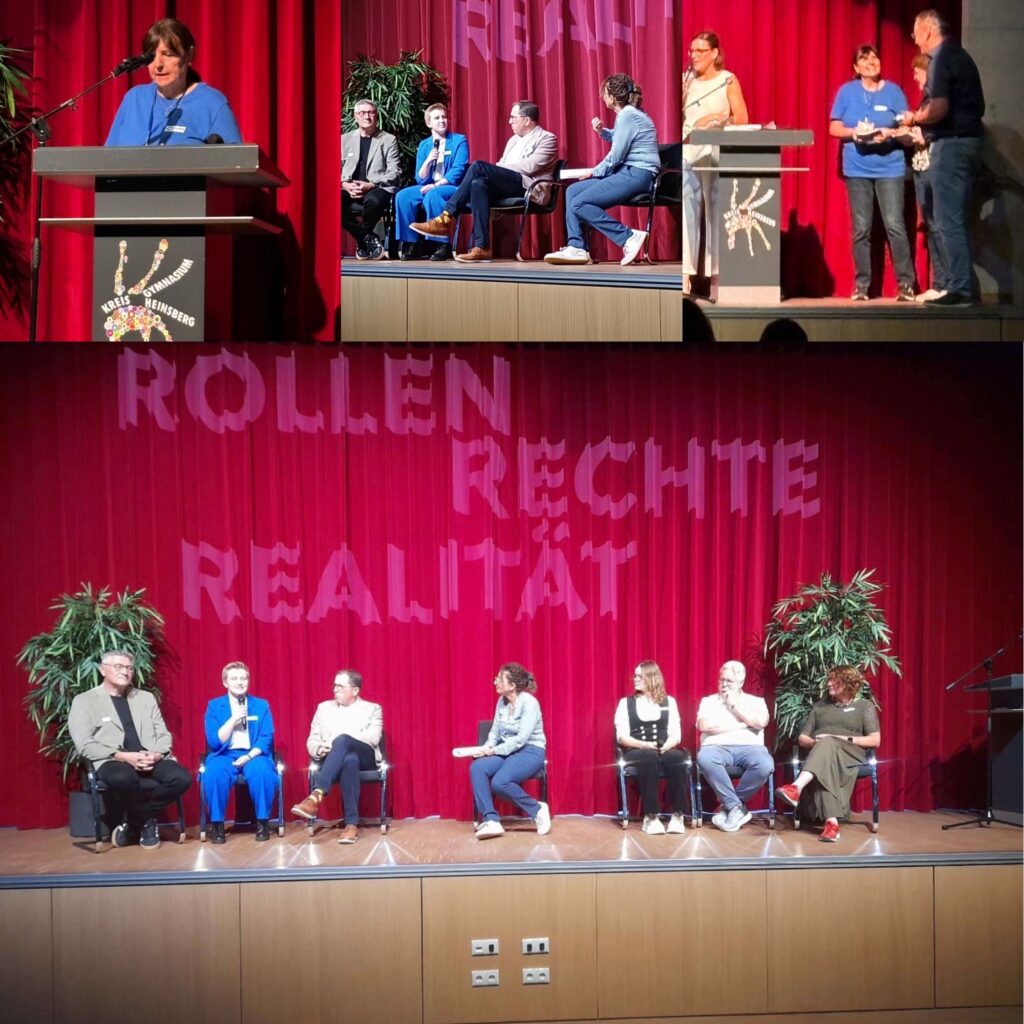 Eine Podiumsdiskussion auf einer Bühne vor einem roten Vorhang mit der Aufschrift ROLLEN RECHTE REALITÄT, an der mehrere Redner teilnehmen, die auf Stühlen und an Rednerpult sitzen.